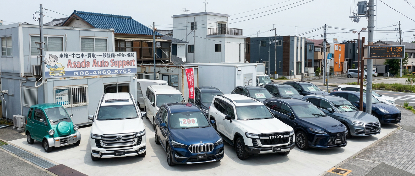 アサダオートサポートの店舗外観。事務所の壁に「車検・中古車・買取・一般整備・板金・保険」と書いた看板があり、前の展示場に車が並んでいます。